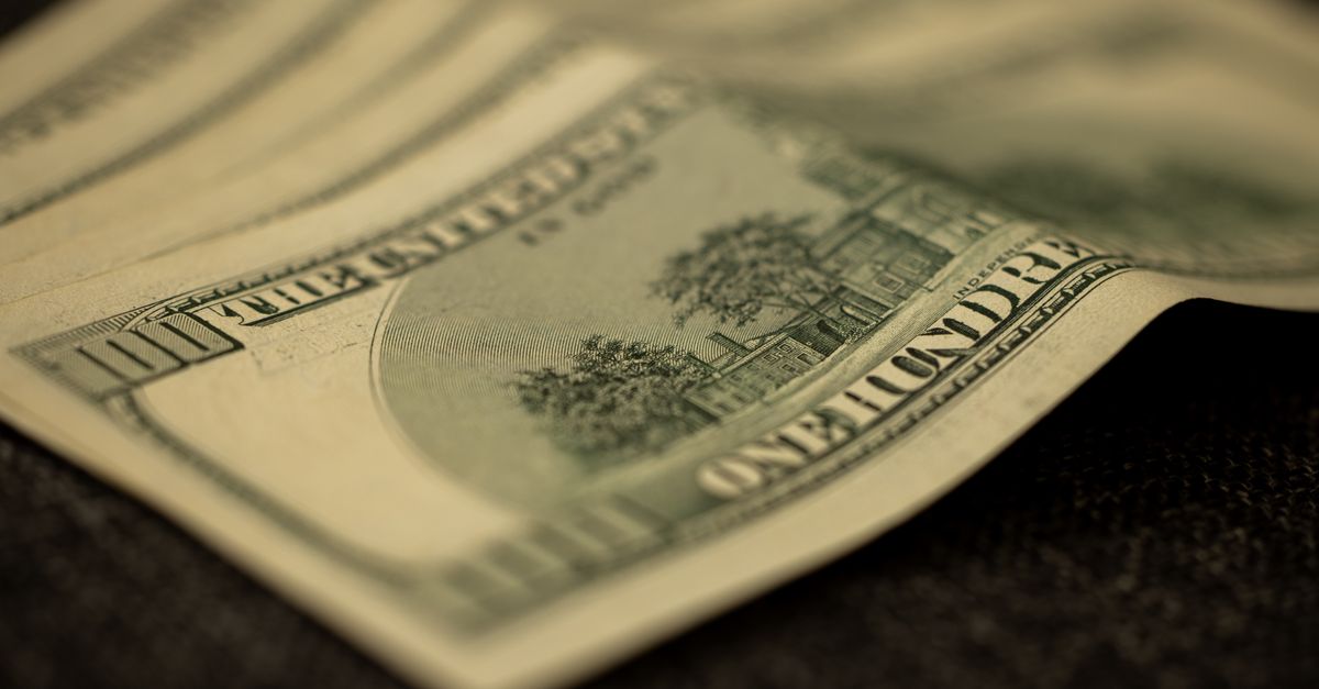 Detailed shot of multiple US hundred dollar bills fanned out on a flat surface, symbolizing wealth.