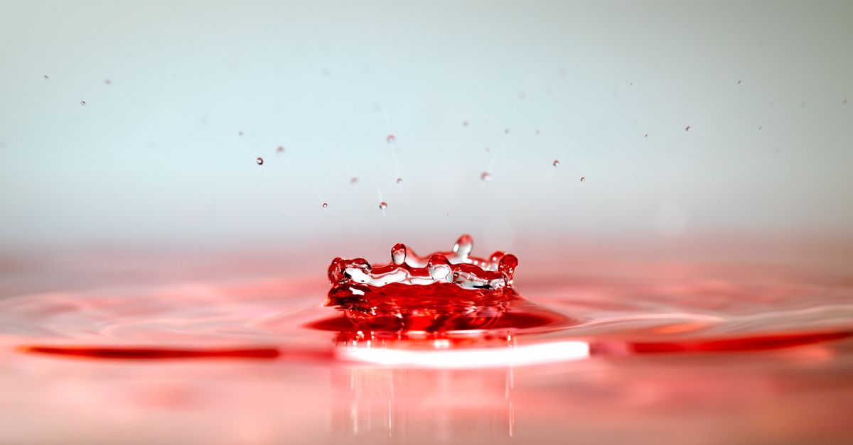 Close-up photo of a red water droplet creating ripples, showcasing fluid dynamics.