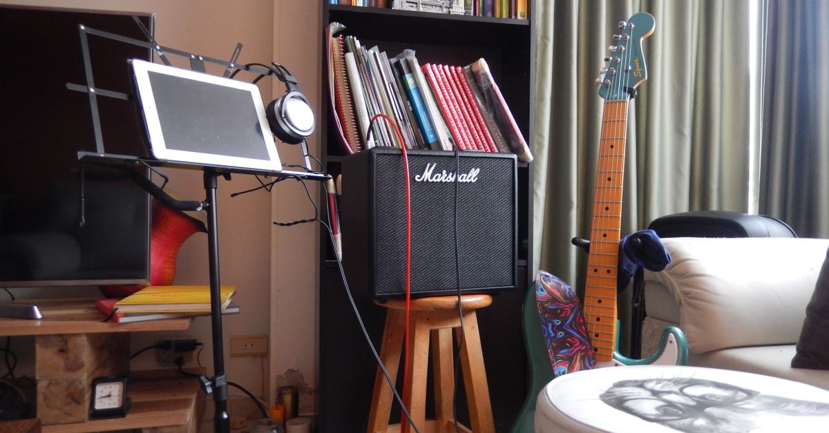 A music room featuring a guitar, amplifier, music stand with tablet, and bookshelf, perfect for musicians.