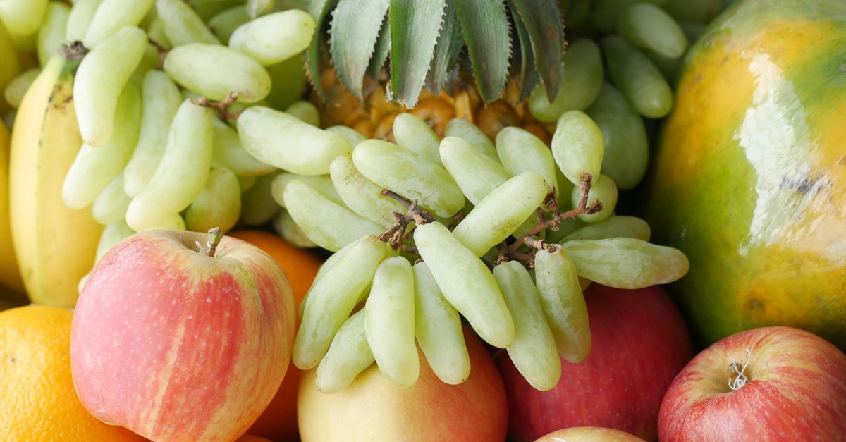 Close-up photo of assorted fresh fruits including apples, oranges, grapes, and pineapple.
