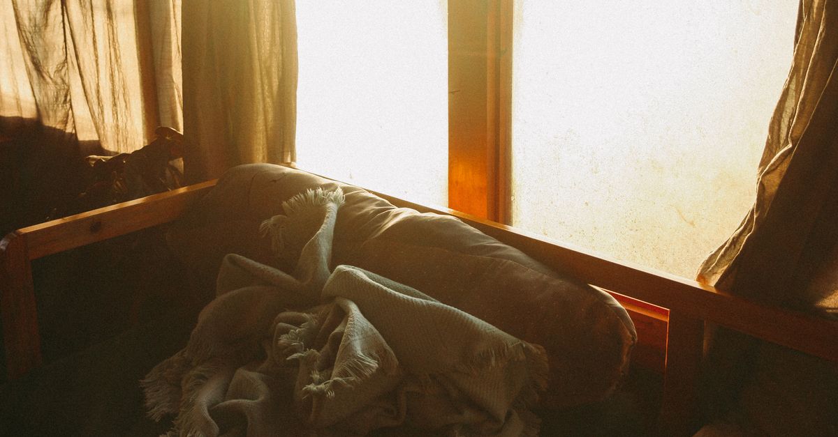 Warm and cozy interior scene with sunlight streaming through a window onto a sofa and blanket.