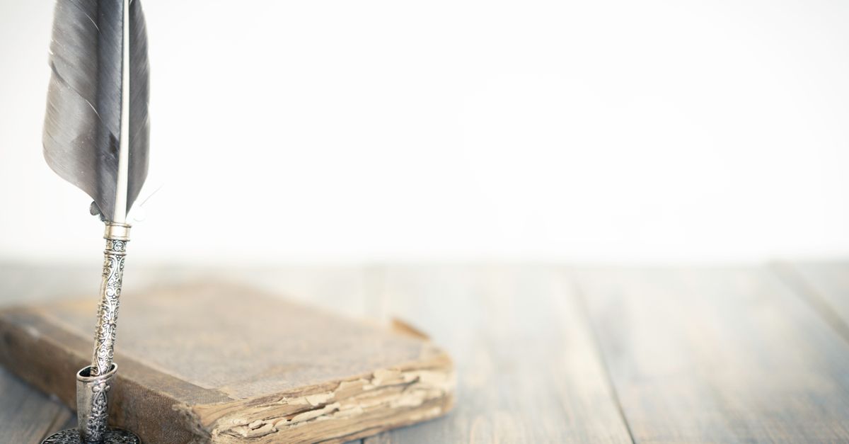 A detailed feather quill beside an aged book on a wooden surface, evoking a classic atmosphere.