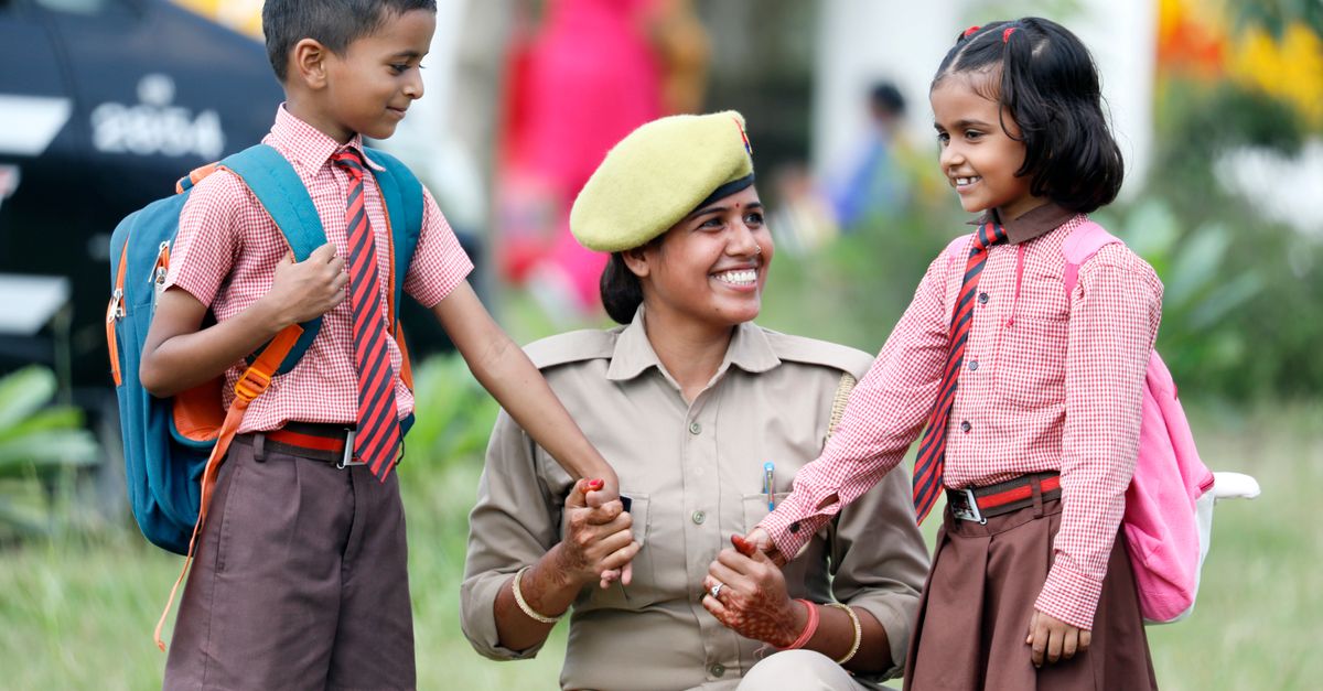 A policewoman smiling and interacting with schoolchildren in uniforms. Outdoors, warm and cheerful scene.