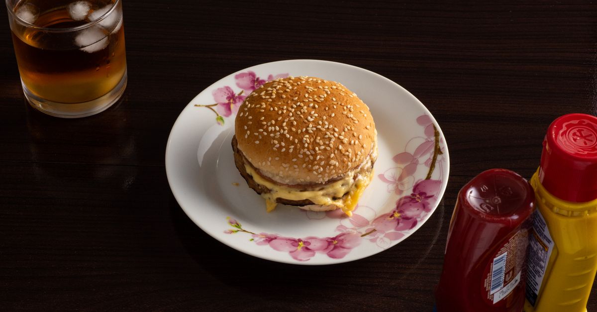 A cheeseburger with condiments and a drink on a dark wooden table.