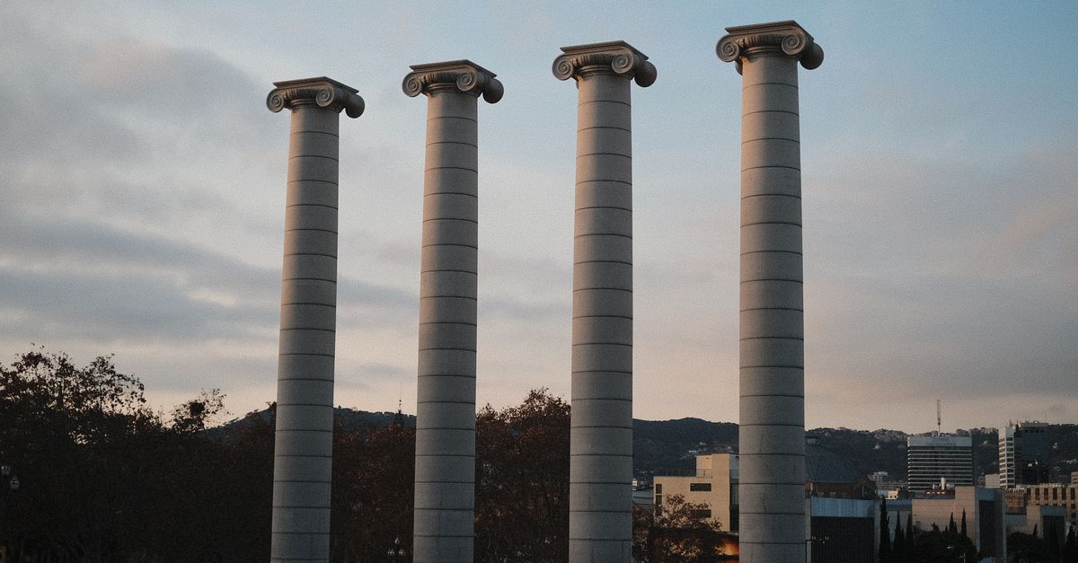 Low-angle view of the iconic four columns at Montjuïc in Barcelona against a serene sky.