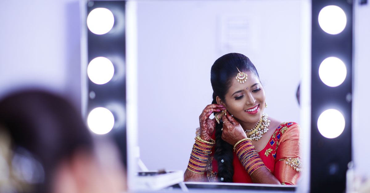 Captivating Indian bride adorned in traditional attire, smiling at her reflection while preparing for a wedding ceremony.