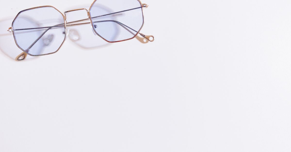 Close-up of hexagonal eyeglasses with blue tint on a white background, minimalistic style.