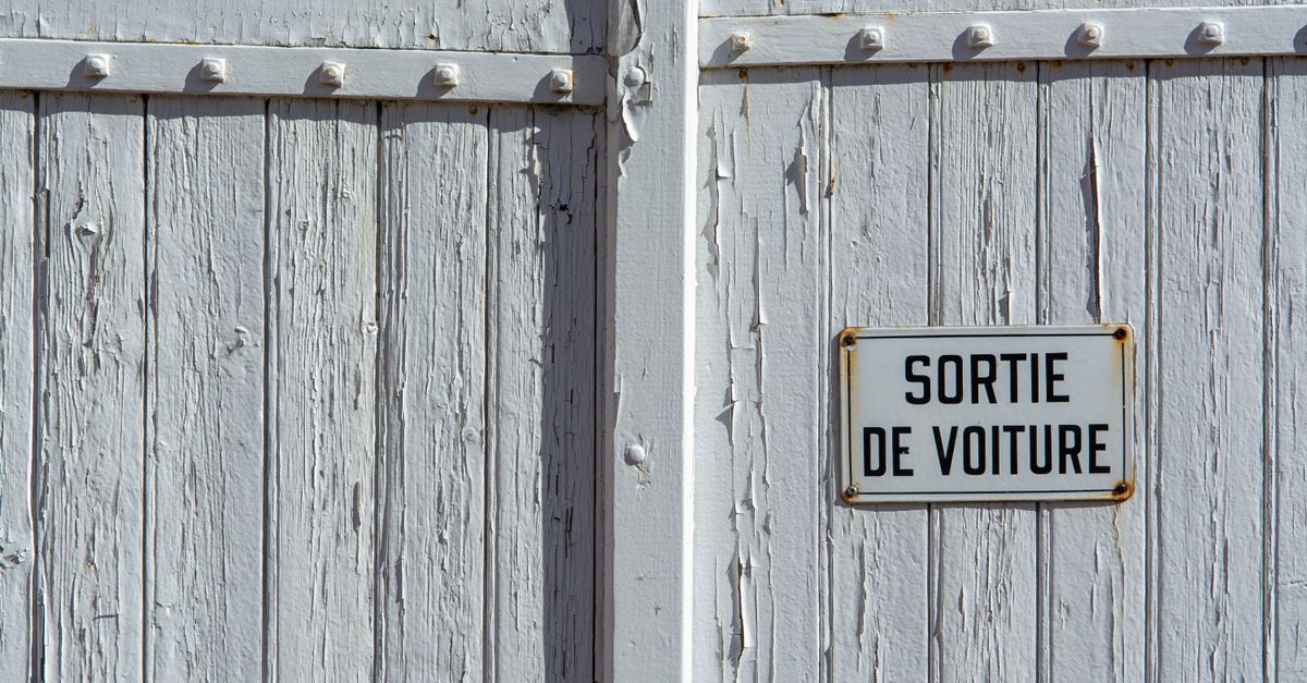 Close-up photo of a weathered wooden wall with a French 'car exit' sign.