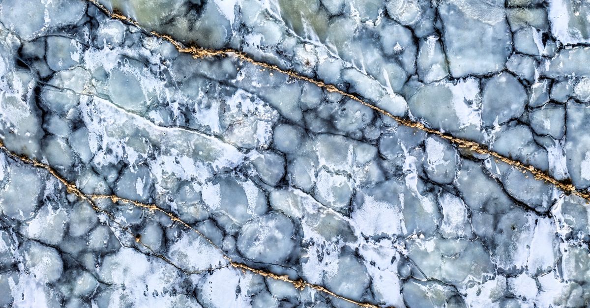 Close-up of an abstract blue ice pattern featuring golden veins, resembling icy stones.