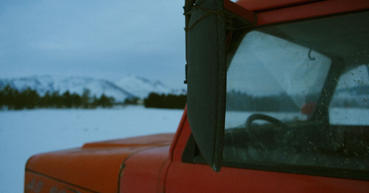 Red truck close-up with snowy winter landscape and mountains.