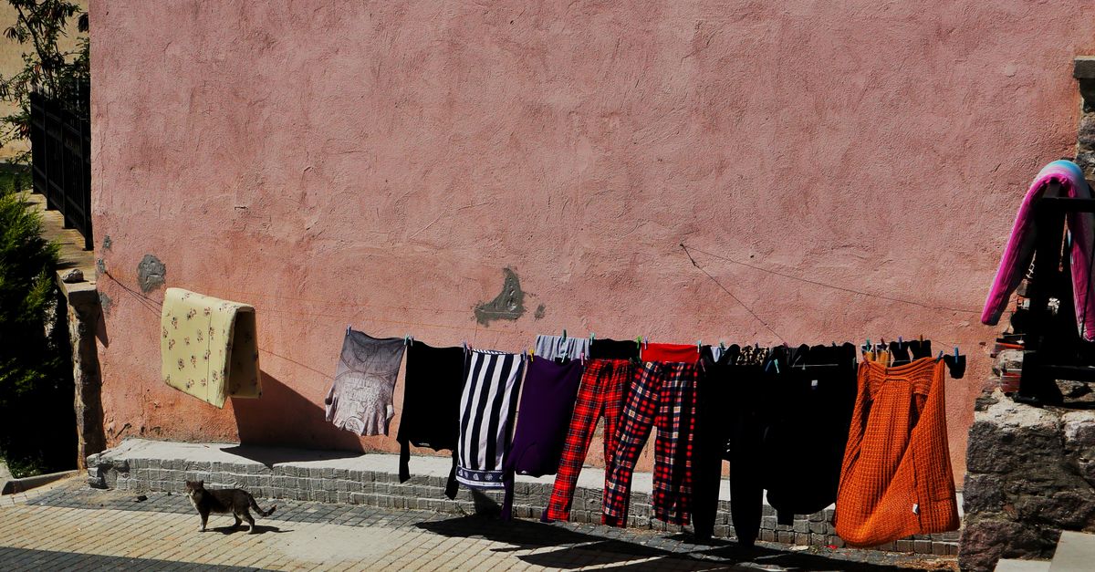 Colorful clothes dry in sunlight on a clothesline, with a cat wandering in a charming urban alley.