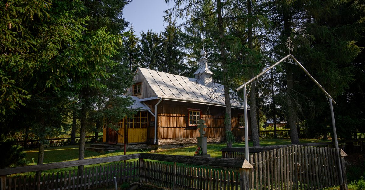 A rustic wooden church surrounded by trees in a secluded rural location, featuring traditional architecture.