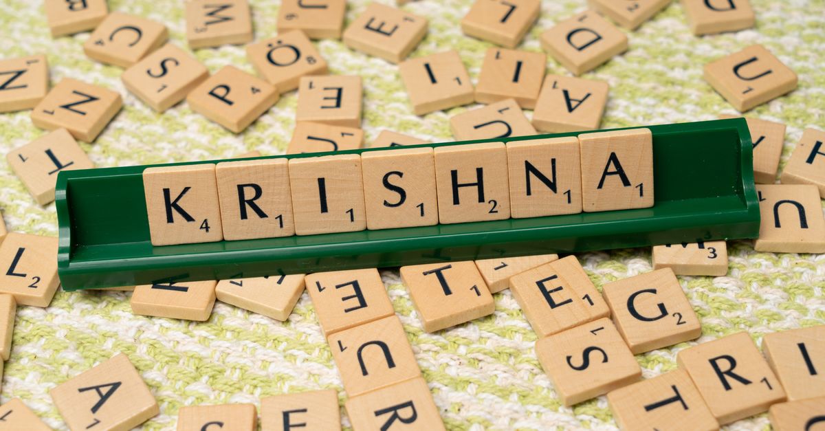 Wooden Scrabble tiles spelling 'Krishna' on a green rack amidst scattered tiles.