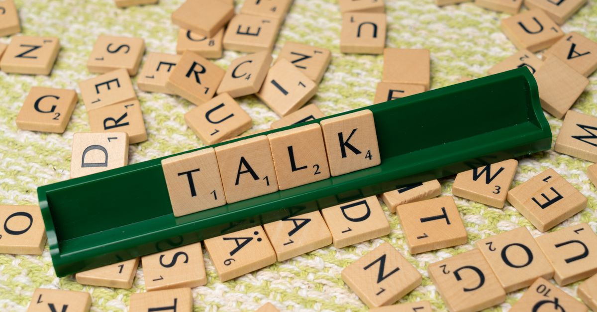 Scrabble tiles arranged to spell 'Talk' on a green tray, surrounded by scattered tiles on a textured surface.