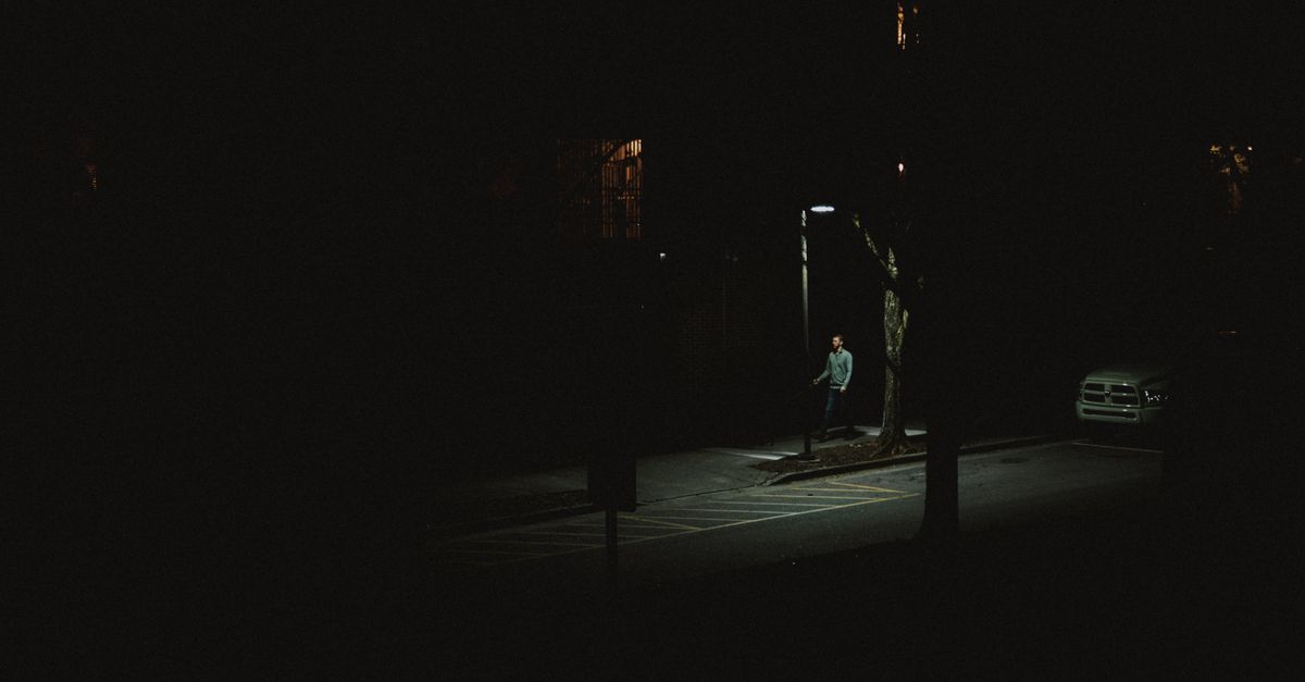 A lone person walking under a streetlight on a dark city street at night.