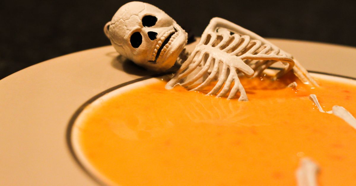 Spooky Halloween-themed pumpkin soup with a toy skeleton for festive decoration.