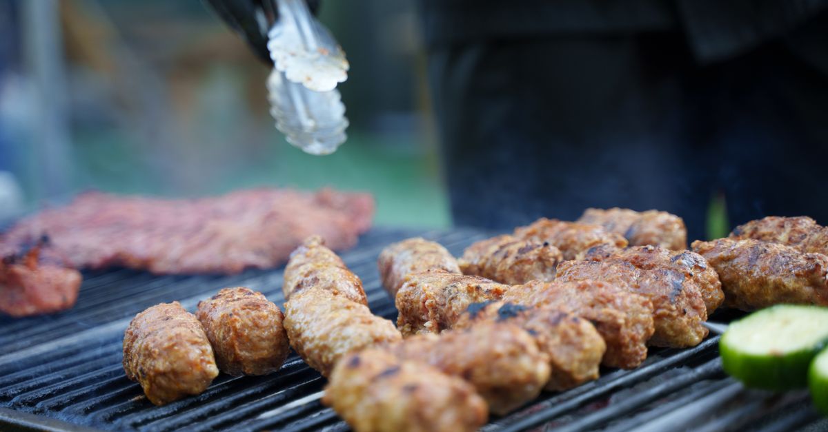 Grilled sausages and meat on a barbecue with tongs and vegetables.