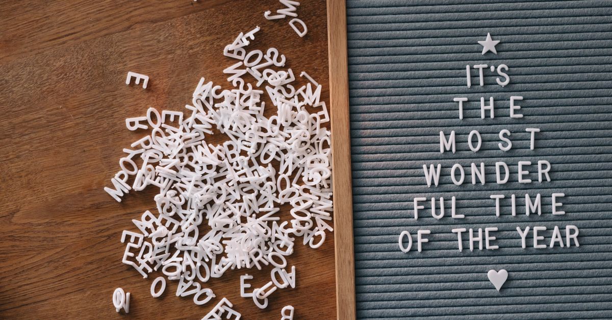 A festive letter board displays a Christmas message with scattered letters on a wooden background.
