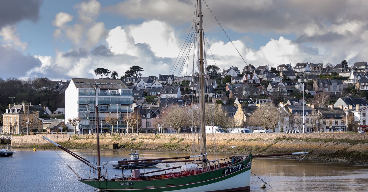 A picturesque view of a vintage sailboat moored at Perros-Guirec harbor with charming French architecture in the background.