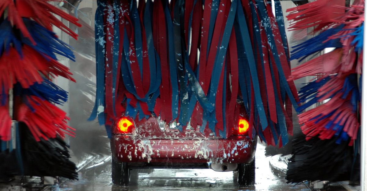 Red car being cleaned in an automated car wash with colorful brushes and soap suds.