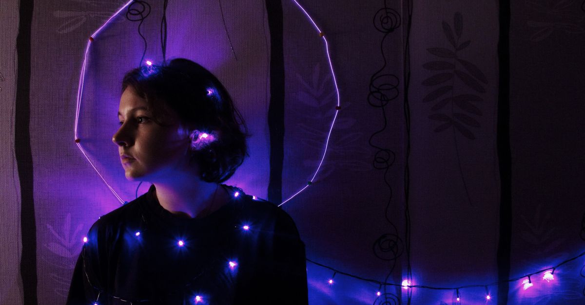 A young woman posing with purple string lights indoors, creating a moody and artistic portrait.