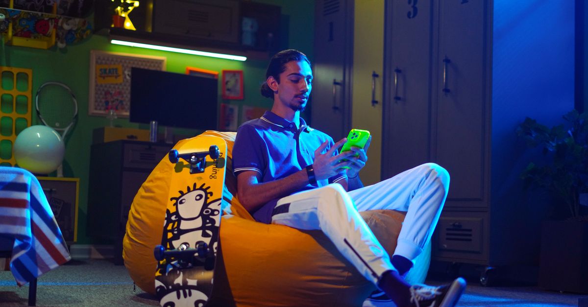Young man in modern room relaxing on a beanbag with a smartphone, beside a skateboard.