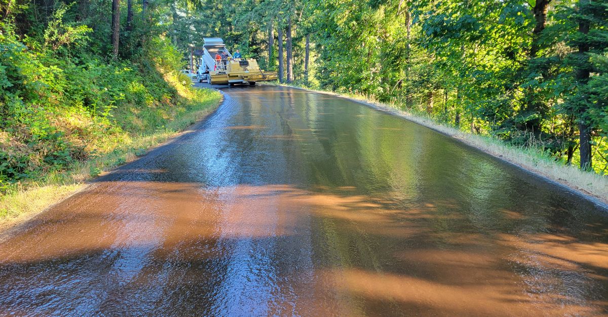 Smooth freshly paved road through lush forest in Sutherlin, Oregon, showcasing summer greenery.
