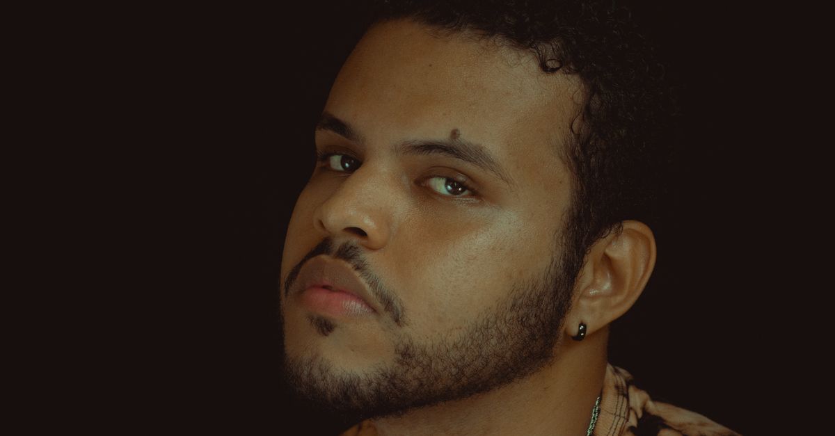 Close-up portrait of a young man with a contemplative expression against a dark backdrop.