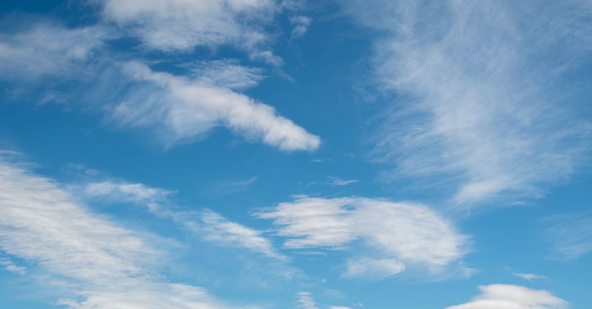 A serene blue sky filled with light, wispy clouds, perfect for nature themes.