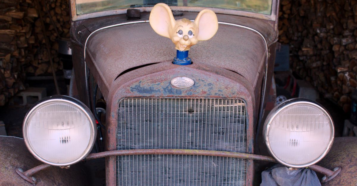Rustic old car with a cheerful mouse hood ornament parked indoors.
