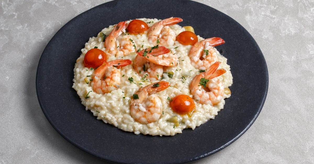 Appetizing shrimp risotto topped with cherry tomatoes on a black plate.