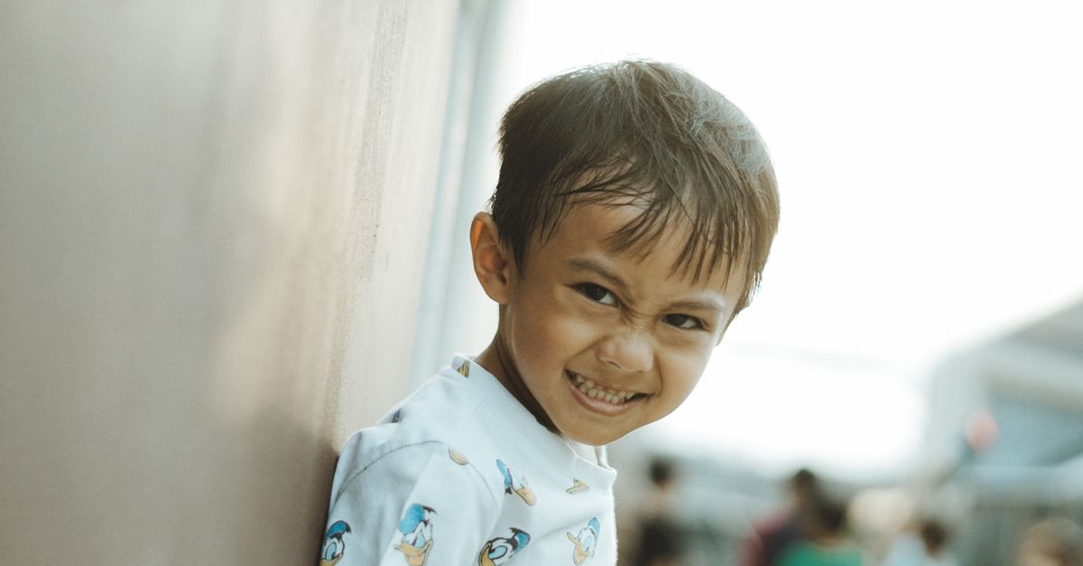 A happy child smiling brightly while leaning on a wall outdoors in West Java, Indonesia.