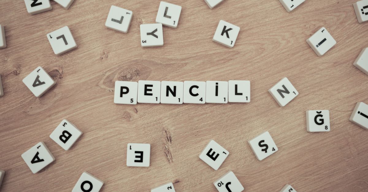 Wooden surface with scattered Scrabble tiles forming the word 'Pencil'.