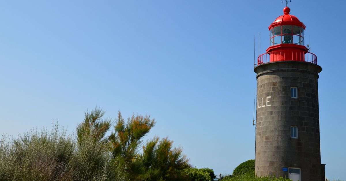A picturesque view of the Granville Lighthouse in Normandie, France against a vibrant blue sky.
