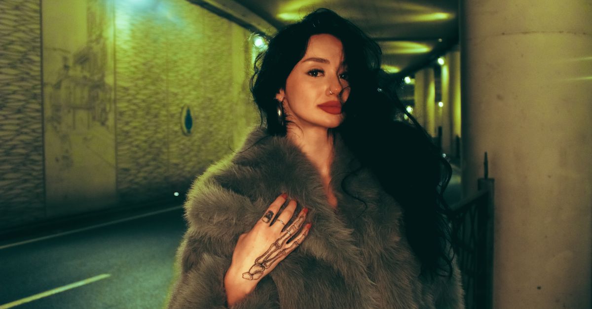 Fashionable woman in faux fur, posing in an urban tunnel at night, exuding confidence.