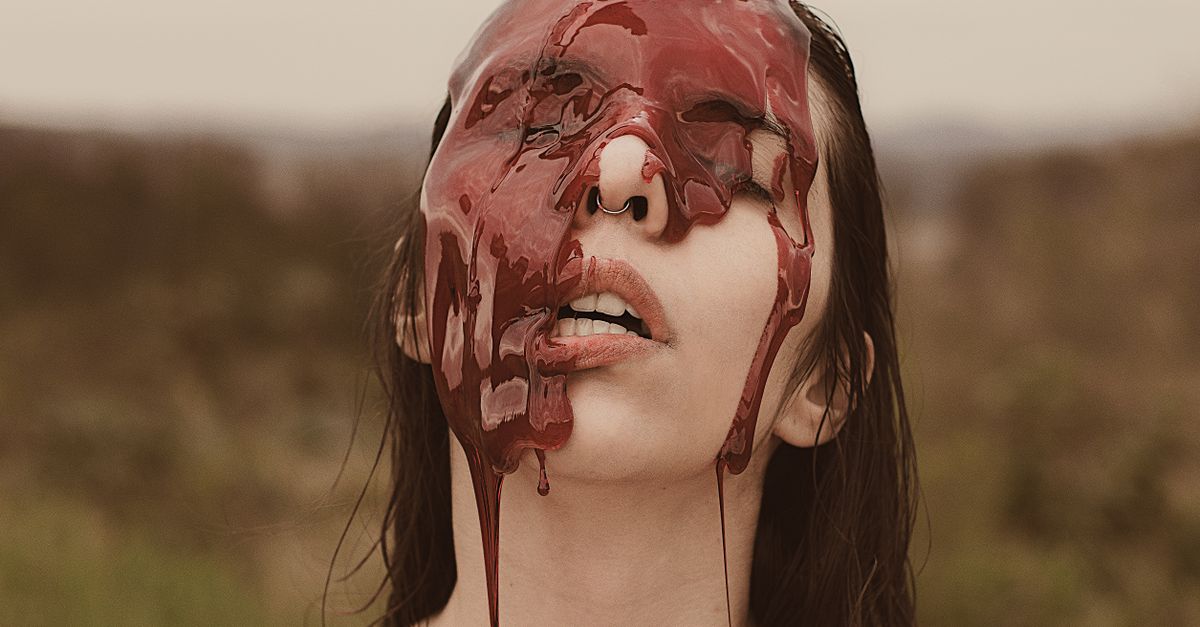 Artistic portrait with red liquid mask on face, depicting a unique conceptual theme outdoors.