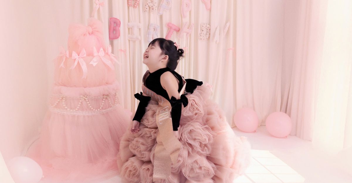 A happy child in a frilly pink dress celebrates a birthday in a pastel-themed room.