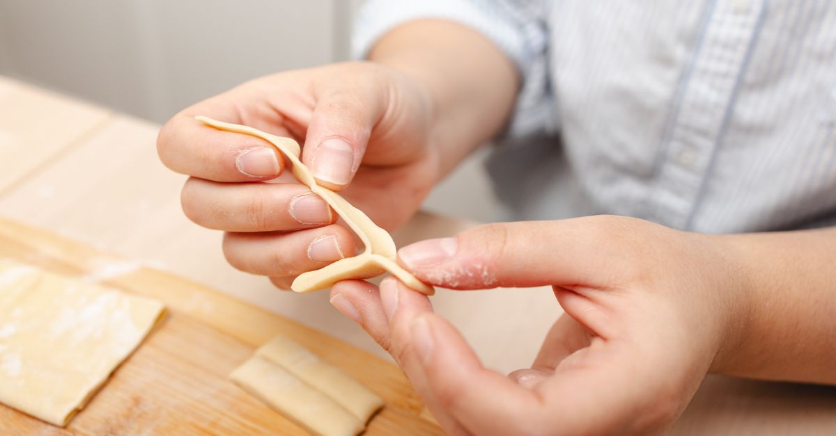 Hands skillfully shape fresh pasta dough on a wooden board in a cozy kitchen scene.