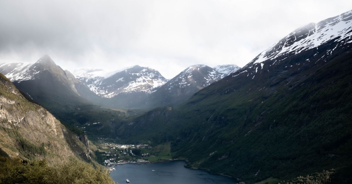 Breathtaking landscape of Geirangerfjord surrounded by snow-capped mountains and lush greenery in Norway.
