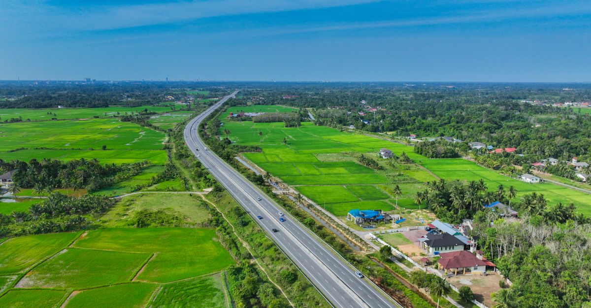 Scenic aerial view of a highway cutting through lush green rice fields in Kota Bharu, Malaysia.