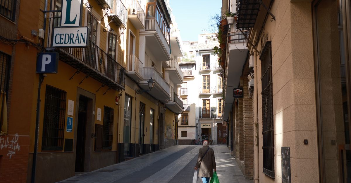 A single person walking along a narrow street surrounded by traditional Spanish architecture.