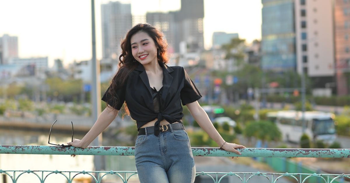 Stylish woman poses on a city bridge with a vibrant urban backdrop.
