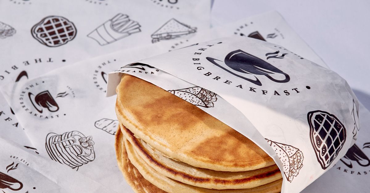 A stack of delicious pancakes wrapped in decorative paper on a breakfast table setting.