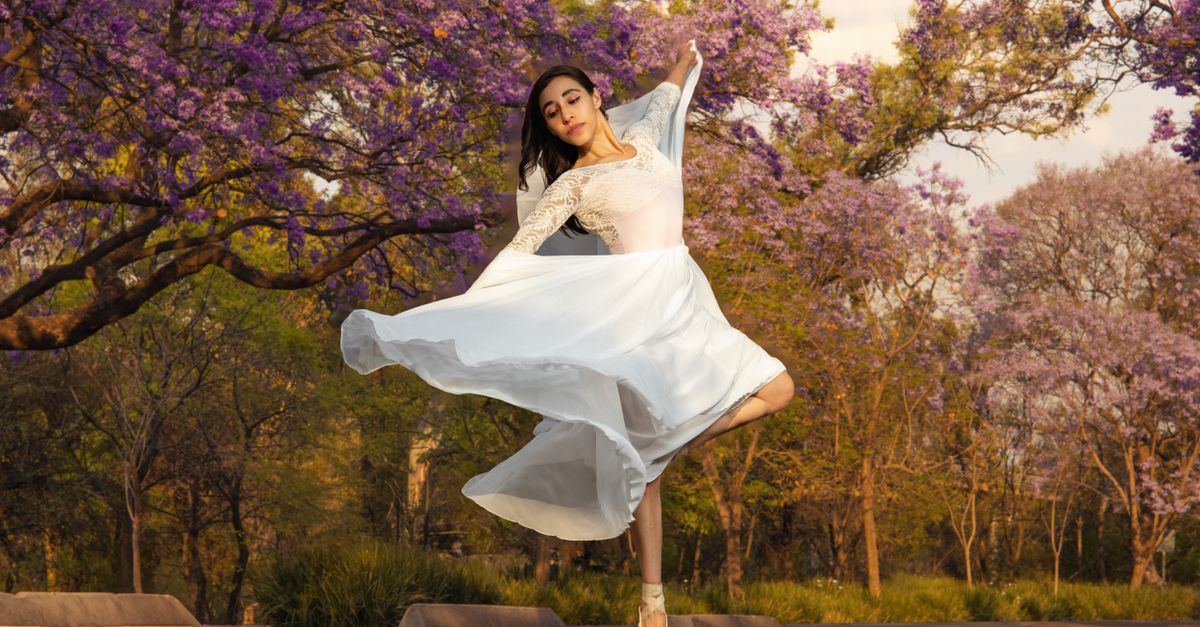 Elegant ballerina in white dress dancing amidst blooming jacaranda trees.