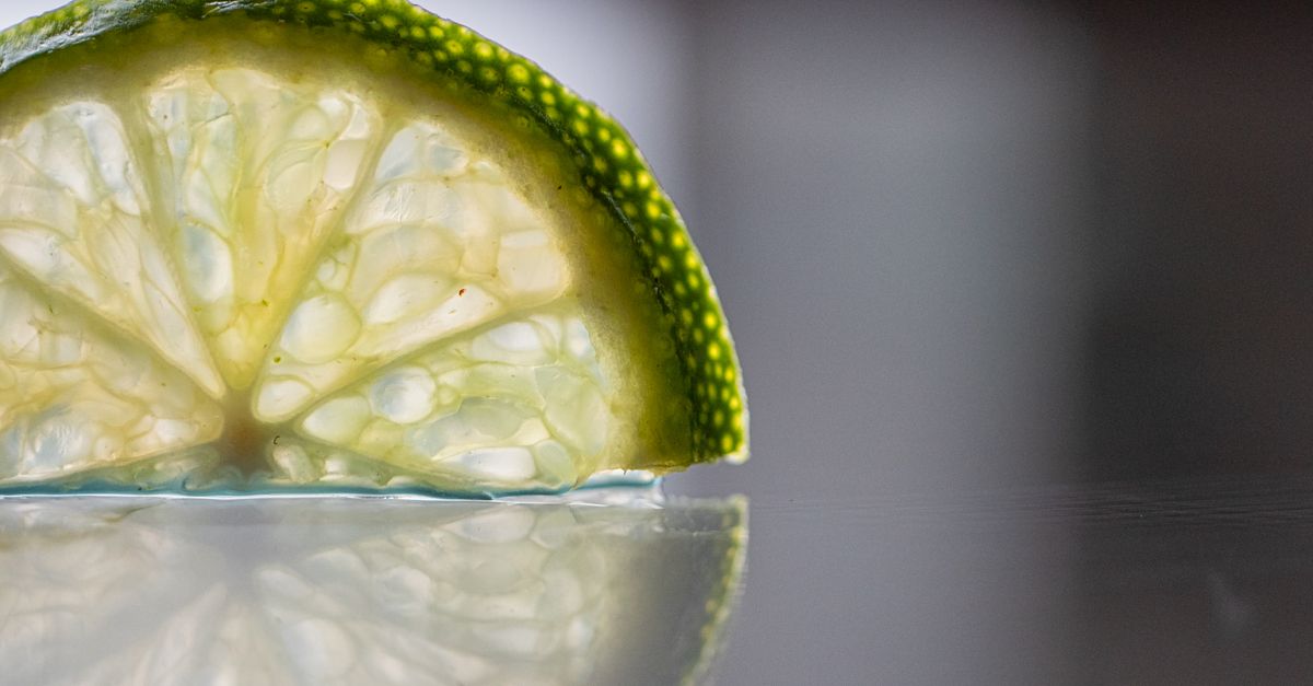 Detailed close-up of a lime slice showcasing its texture with a clear reflection on a smooth surface.