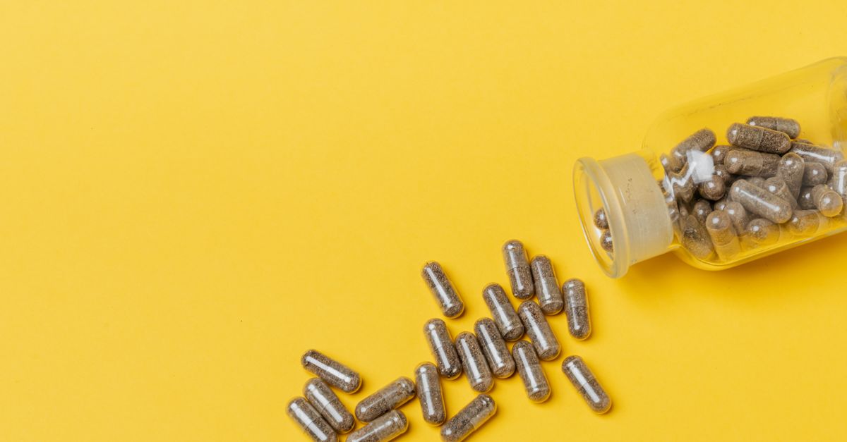 Close-up of spilled capsules from a bottle on a vibrant yellow background.