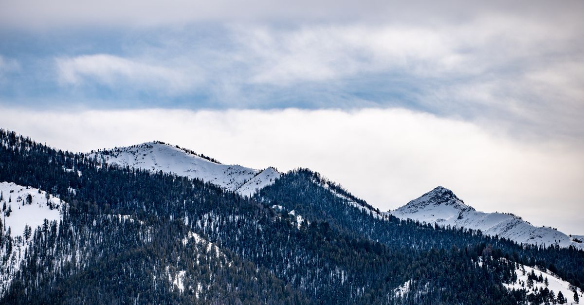 Dramatic winter landscape of snow-capped mountains under a cloudy sky.