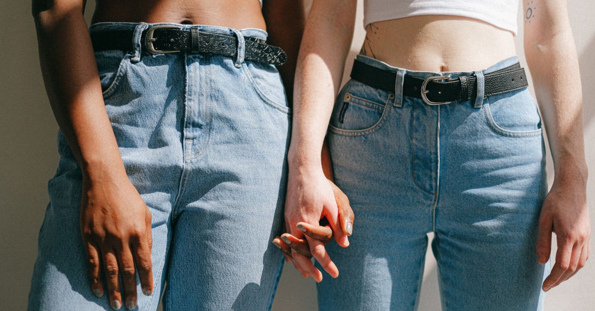 Close-up of interracial lesbian couple holding hands, expressing love and diversity in denim outfits.