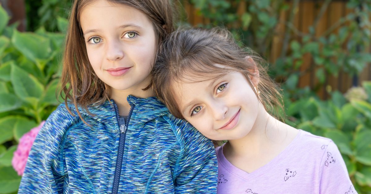 Grinning young girls with brown hair and bright eyes in casual clothes standing next to each other and looking at camera