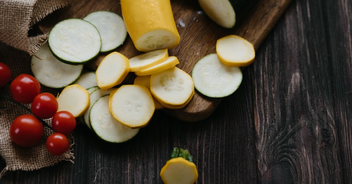 A selection of sliced zucchini and cherry tomatoes on a rustic wooden board, highlighting fresh and organic ingredients.
